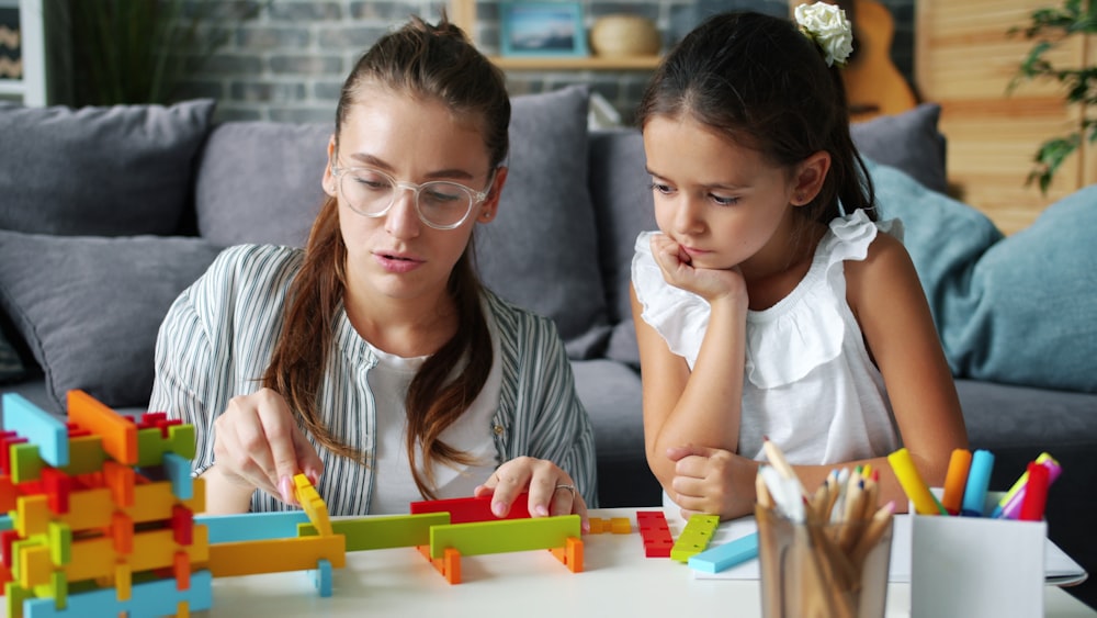 A caregiver and a young girl building with coloured blocks at a table.