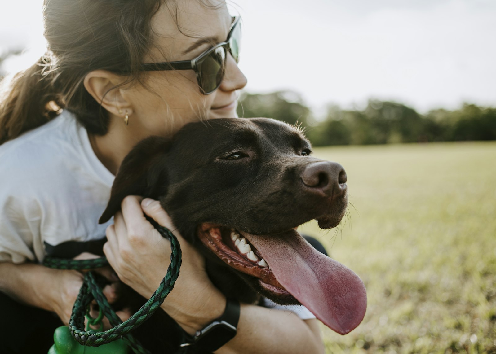 A woman smiling as she hugs a happy dog in a park.