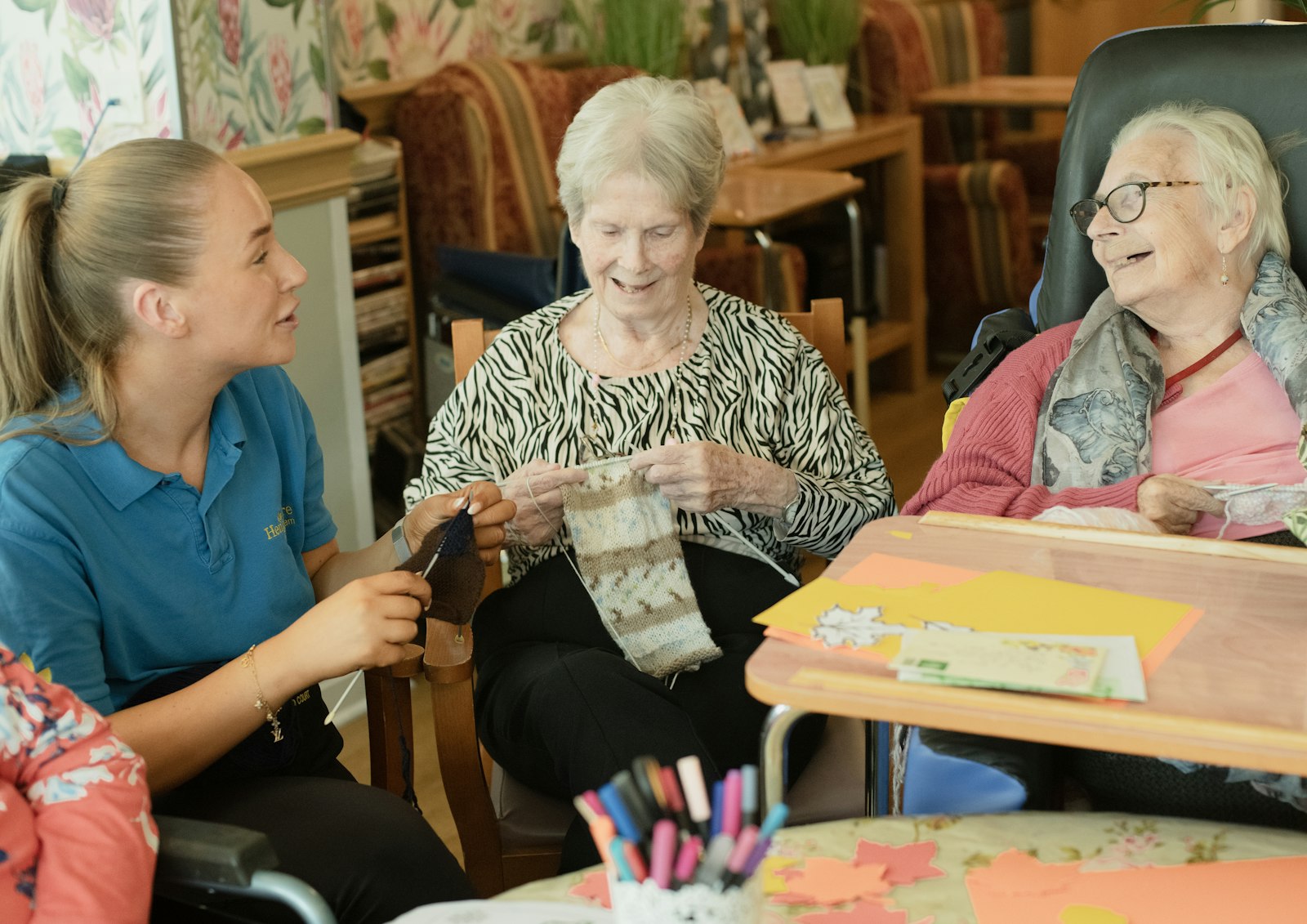 A caregiver knitting with two older women, all smiling.