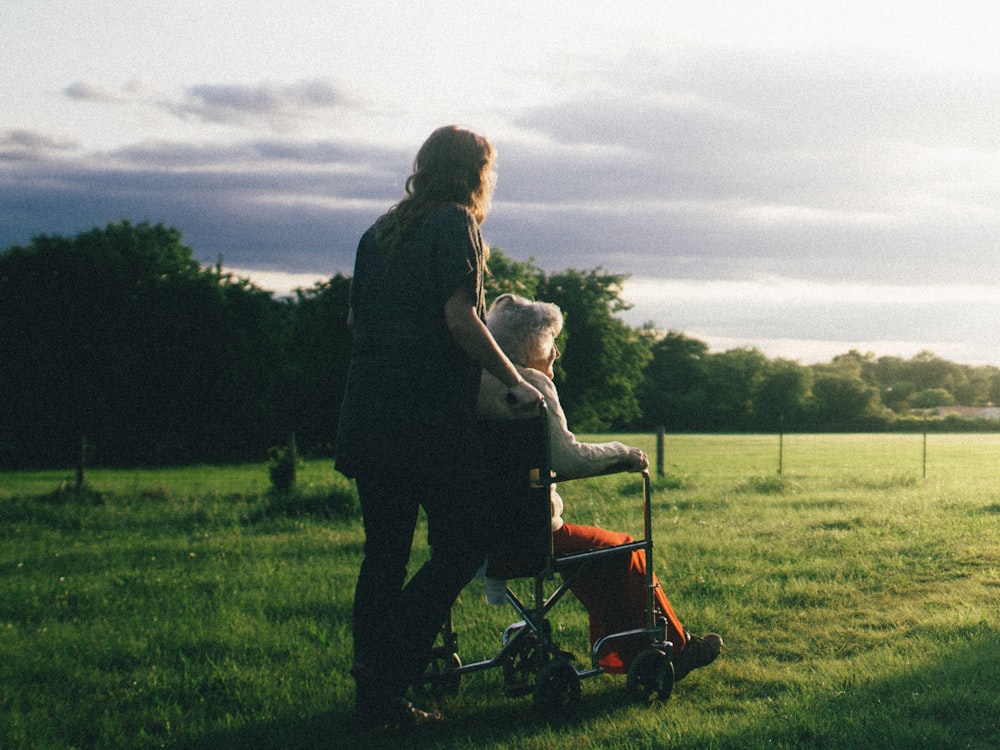 A companion walking with someone in a wheelchair across a field at sunset.